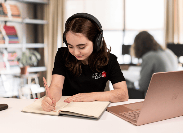 Une adolescente concentrée, assise à son bureau, étudie et écrit des notes pendant une session de tutorat en ligne de La 2e Classe. Cette image illustre son engagement et sa détermination à exceller avec le soutien de nos cours personnalisés.