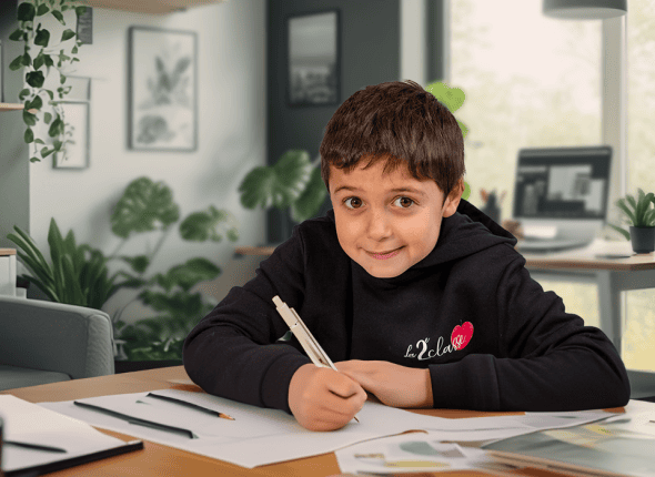 Un petit garçon, concentré et appliqué, écrit dans son cahier durant un cours de La 2e Classe. Assis dans une salle de classe lumineuse, il illustre l'implication des jeunes élèves dans leur éducation continue.