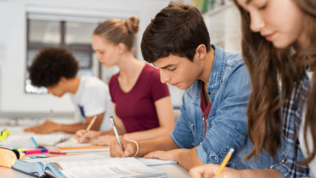 Groupe d'élèves concentrés en train de passer un examen en classe, prenant des notes et remplissant un cahier. Étudiants en pleine révision et évaluation scolaire.