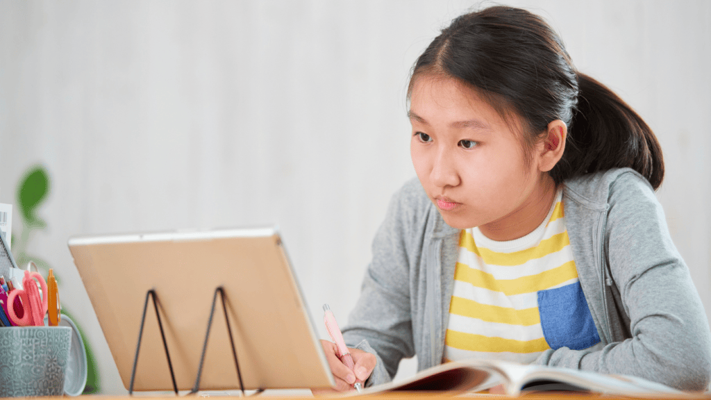 Élève concentrée devant une tablette en train d’étudier et de prendre des notes, représentant l’école en ligne et l’apprentissage à distance.