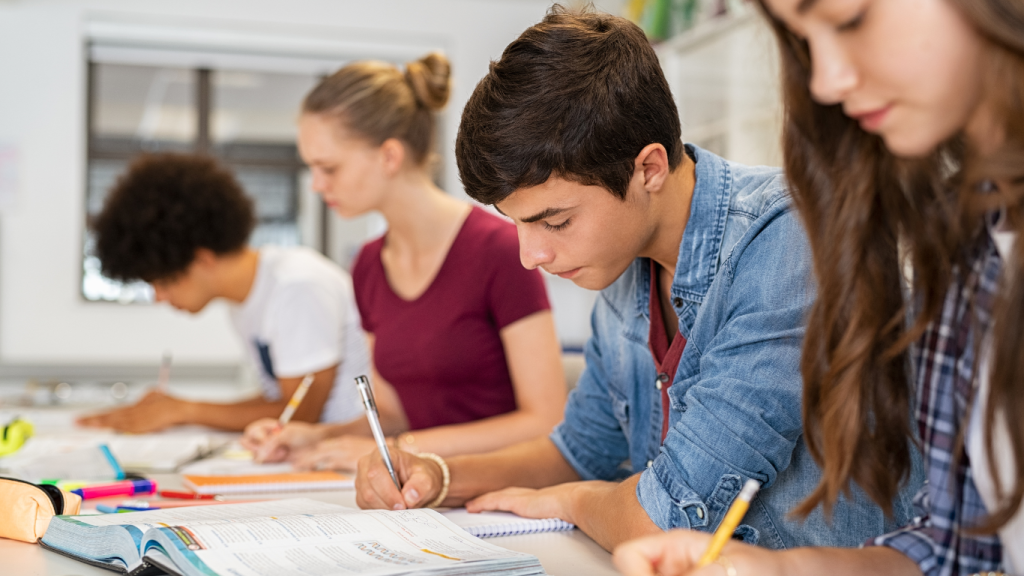 Groupe d'élèves concentrés en train de passer un examen en classe, prenant des notes et remplissant un cahier. Étudiants en pleine révision et évaluation scolaire.