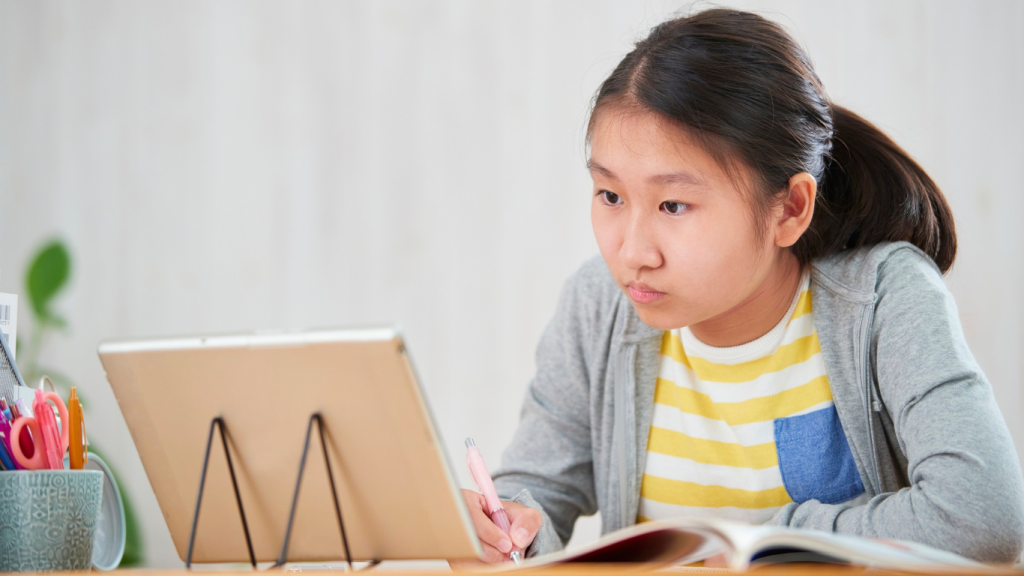Élève concentrée devant une tablette en train d’étudier et de prendre des notes, représentant l’école en ligne et l’apprentissage à distance.