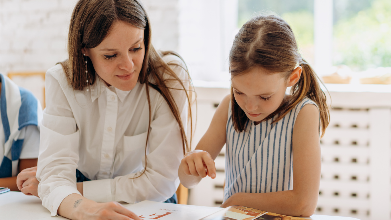 Enseignante accompagnant une jeune élève dans son apprentissage de la lecture, illustrant le soutien scolaire personnalisé.